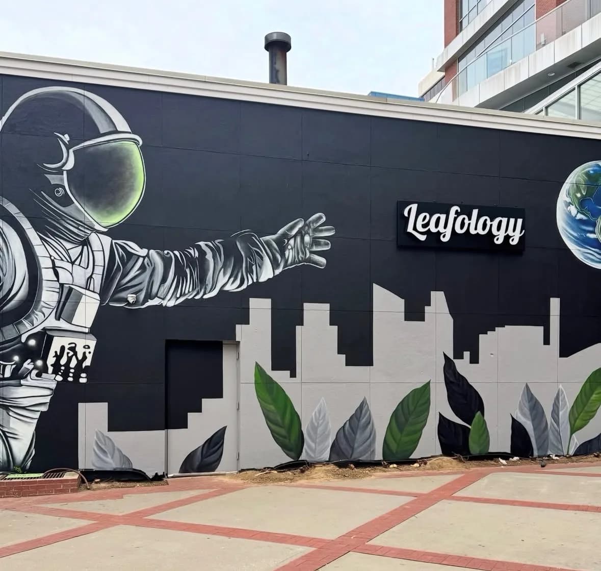 Leafology side-wall astronaut mural reaching toward Earth with cityscape and leaf silhouettes