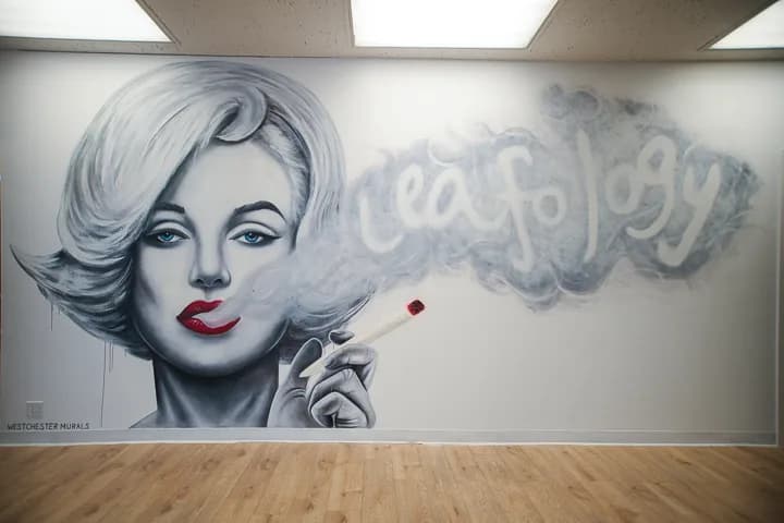 Black-and-white mural of Marilyn Monroe exhaling smoke that spells 'leafology'