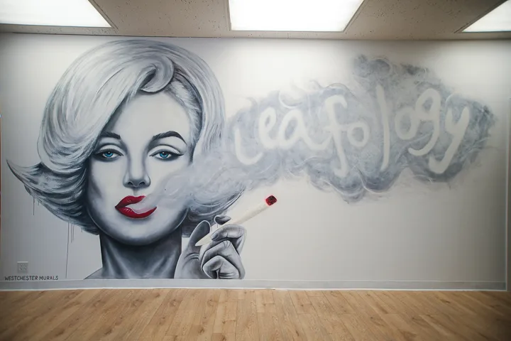 Black-and-white mural of Marilyn Monroe exhaling smoke that spells 'leafology'